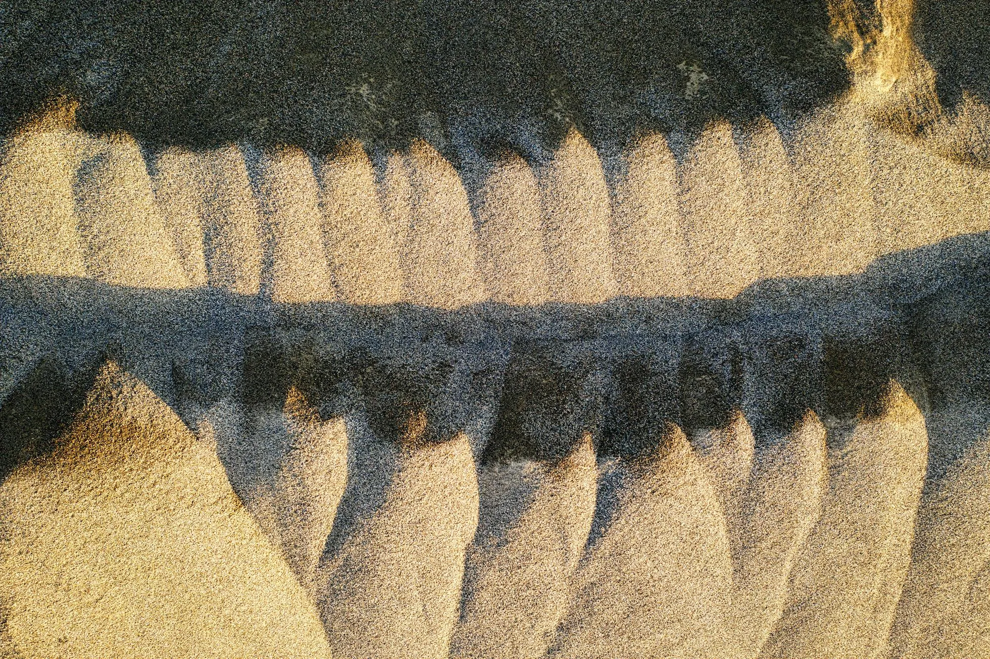 Top-down aerial of two parallel ridges in sand casting long shadows across the surface